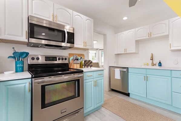 A modern kitchen with white and light blue cabinetry, stainless steel appliances, and a beige rug.