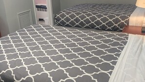 A hotel room with two beds, each with a patterned bedspread. There is a nightstand with a lamp, and a door leading to a bathroom with a towel rack. - Southland Motor Lodge (Brownstown Township)