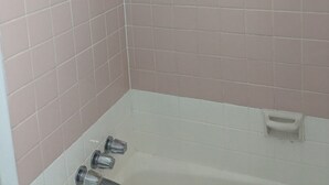A corner of a bathroom with pink tiles, a showerhead, and a bathtub. - Southland Motor Lodge (Brownstown Township)