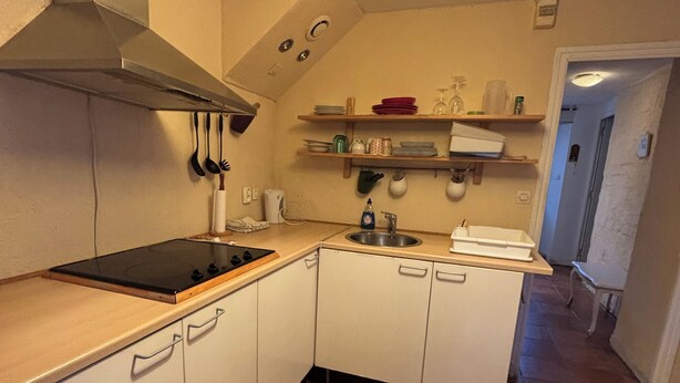 A compact kitchen with white cabinets, a stove, and a hanging light fixture.