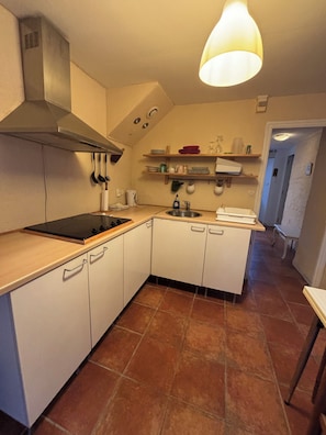 A compact kitchen with white cabinets, a stove, and a hanging light fixture.