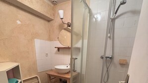A compact bathroom with a glass-enclosed shower, a white sink, and a small shelf unit.