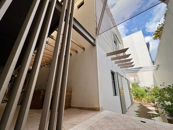 A narrow outdoor corridor with a tiled floor, a white wall, and a metal mesh structure. - NOMADIK HOSTEL (Puebla)