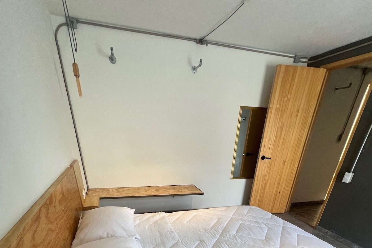 A bed with a wooden headboard, a white quilt, and a wooden shelf above it.