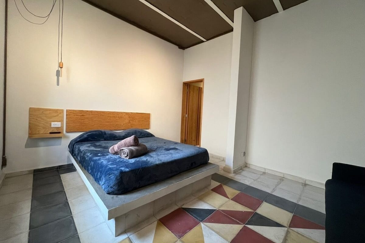 A bedroom with a bed, a wooden headboard, a tiled floor, and a door.