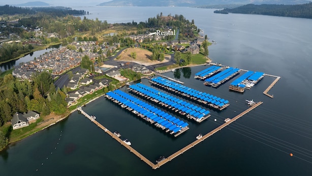 Vue aérienne d’une propriété locative située au bord d’un lac, avec plusieurs bateaux amarrés, une marina et des immeubles résidentiels.