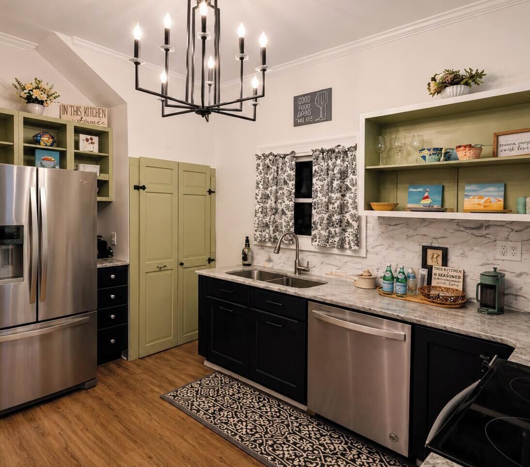 A modern kitchen with a stainless steel refrigerator, a built-in dishwasher, a chandelier, and a window with floral curtains.