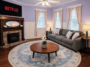 Una sala de estar con chimenea, un sofá, una mesa de centro y un televisor mostrando 'NETFLIX'.