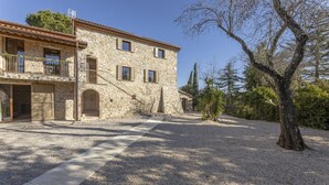Un bâtiment en pierre doté d’un balcon, d’une allée gravillonnée et d’un arbre.