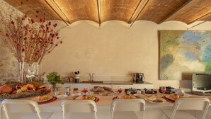 Un coin repas avec une longue table dressée pour quatre personnes, un vase de fleurs séchées et un tableau accroché au mur.
