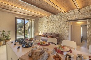 A dining area with a stone wall, wooden ceiling, and a table set with food and drinks. - Antenata | Tuscan farmhouse apartment with pool and nature views (Prata)