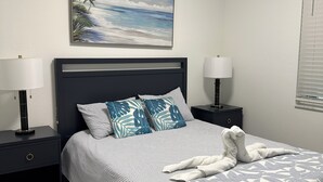 A neatly made bed with a patterned bedspread, two bedside tables with lamps, a wall-mounted painting, and a window with blinds. - Brand-new construction furnished with new items of 2/2 condo  Lakewood Ranch, FL (Lakewood Ranch)
