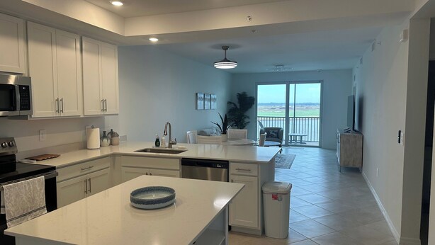 A modern kitchen with white cabinetry, a central island, and a view to a balcony. - Brand-new construction furnished with new items of 2/2 condo  Lakewood Ranch, FL (Lakewood Ranch)