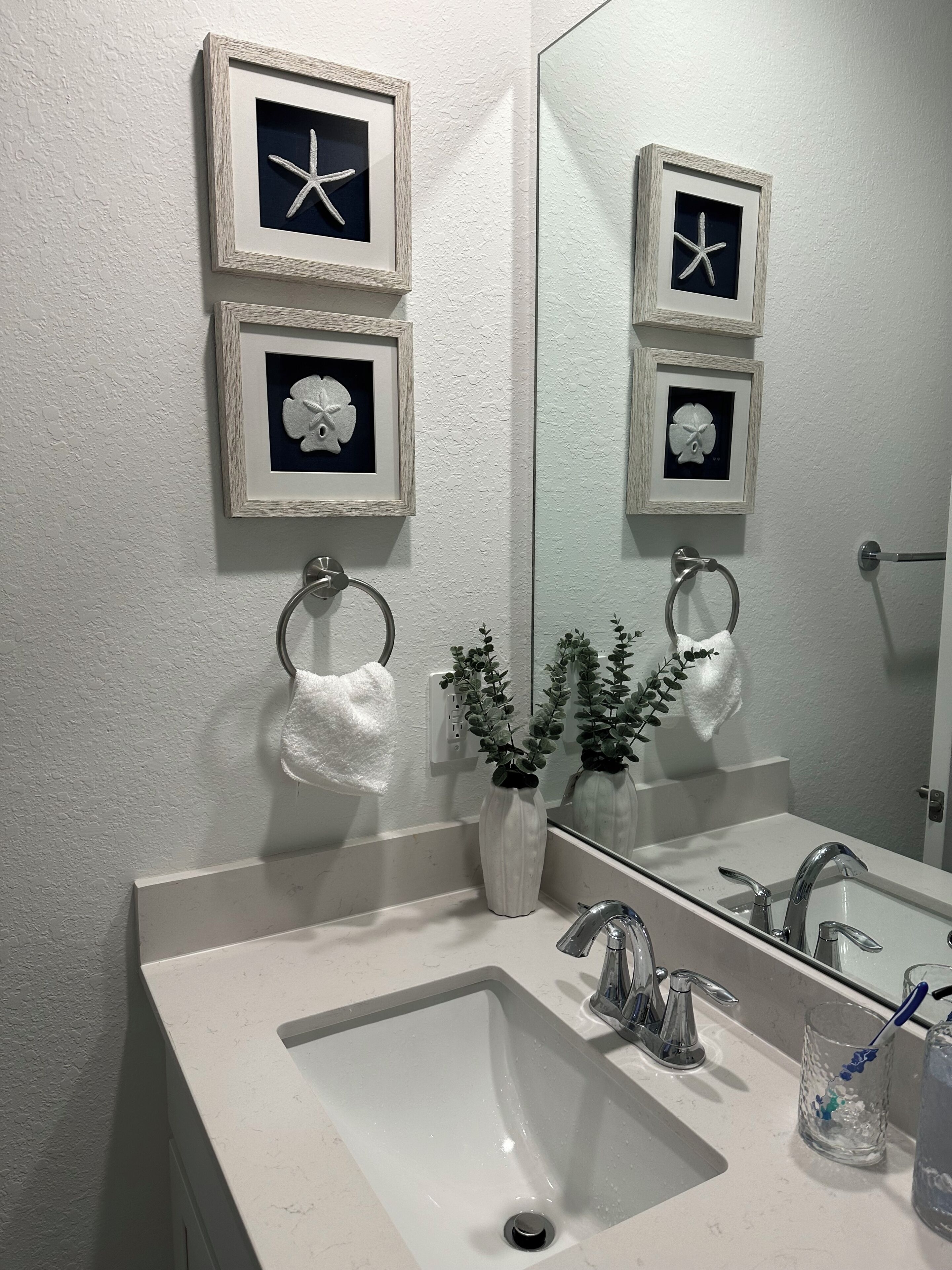 A bathroom with a white sink, two framed starfish decorations, a mirror, and a towel ring.