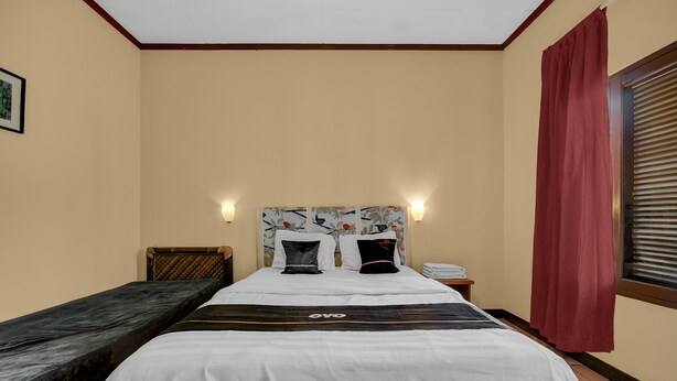 Una habitación de hotel con cama, una mesita auxiliar, una mesita de noche y una ventana con cortinas.