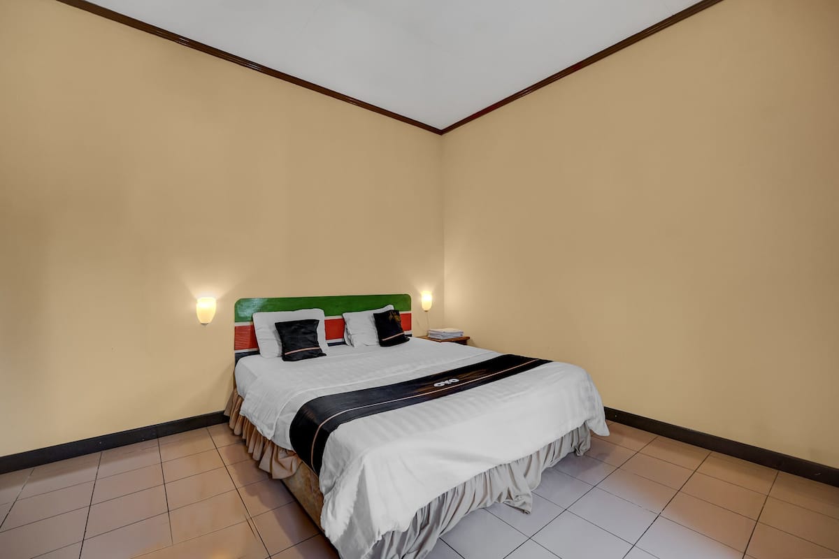 Una cama bien hecha con colcha blanca y negra, cabecera verde y dos mesitas de noche fijadas a la pared.