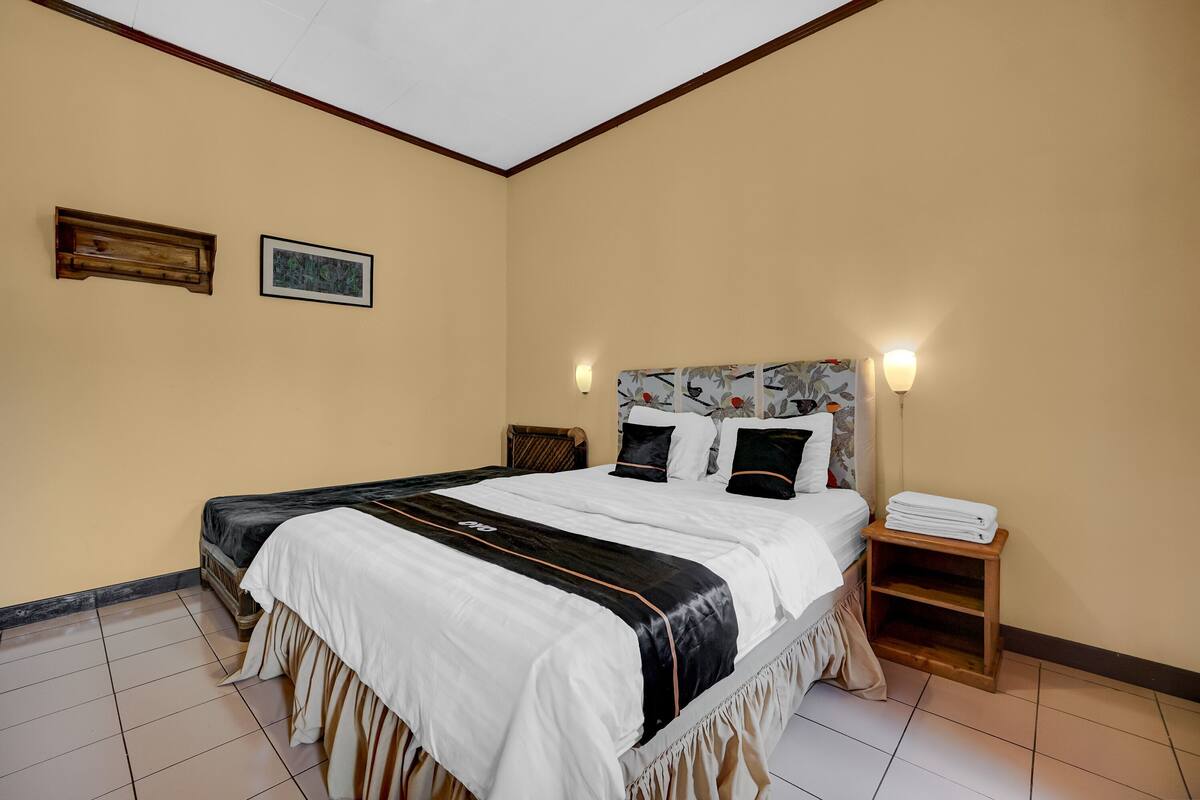 Un dormitorio ordenado con una cama grande, una mesita de noche y dos lámparas fijadas a la pared.