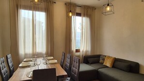 Ein Essbereich mit Holztisch, gedeckt für vier Personen, umgeben von Ledersesseln. In der Ecke befindet sich ein grünes Sofa und ein kleiner Tisch mit Kissen.