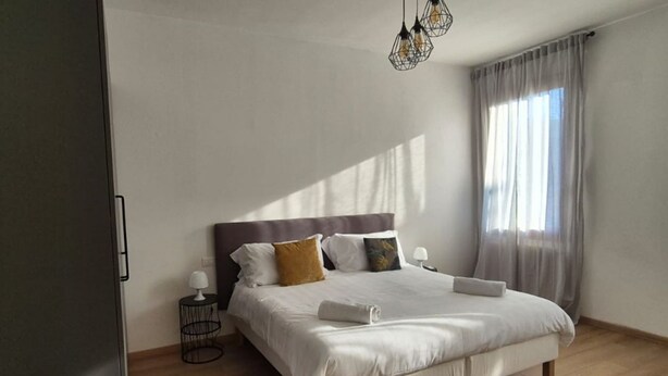 Ein modernes Schlafzimmer mit einem großen Bett, einem Nachttisch, einer Lampe und einem Fenster mit Vorhängen.