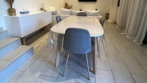 Ein moderner Essbereich mit einem langen Tisch, Stühlen, einem an der Wand befestigten Fernseher und einer Treppe, die zu einer oberen Ebene führt.
