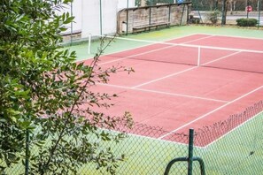 Un campo da tennis con rete, circondato da una recinzione a rete metallica e vegetazione.
