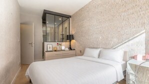 Een moderne slaapkamer met een groot bed, een nachtkastje met lamp en een spiegel erboven.