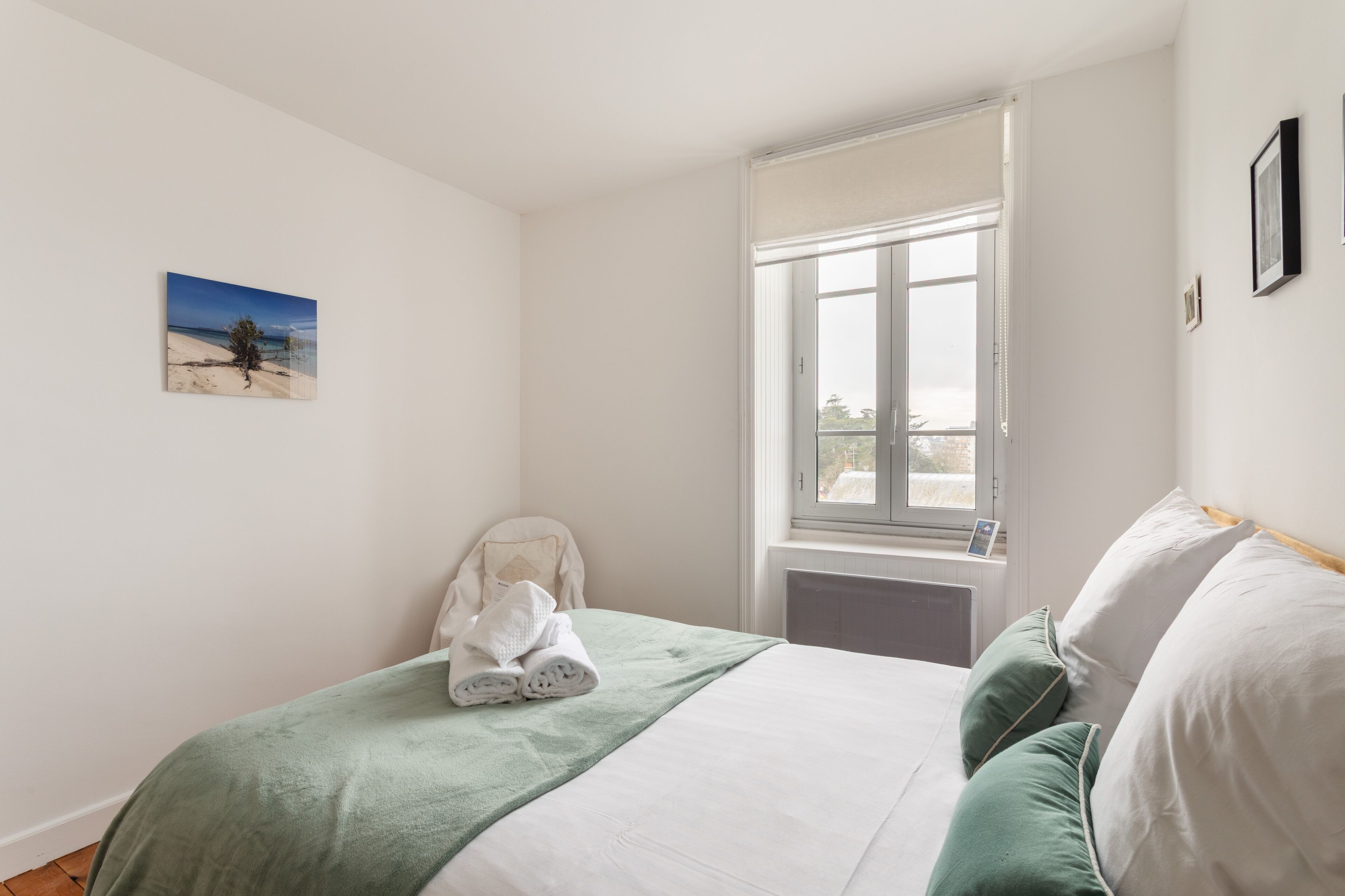 Una camera da letto con un letto, una finestra, un asciugamano e un quadro appeso al muro.