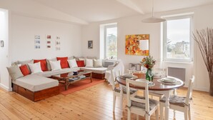 En moderne stue med sofa, spisebord og stole. Vinduer giver naturligt lys og udsigt over byen.