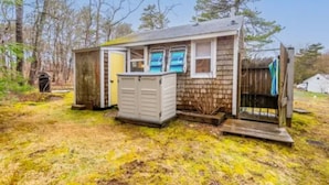 Une petite cabane en bois, de plain-pied, avec une porte, des fenêtres et un petit porche.