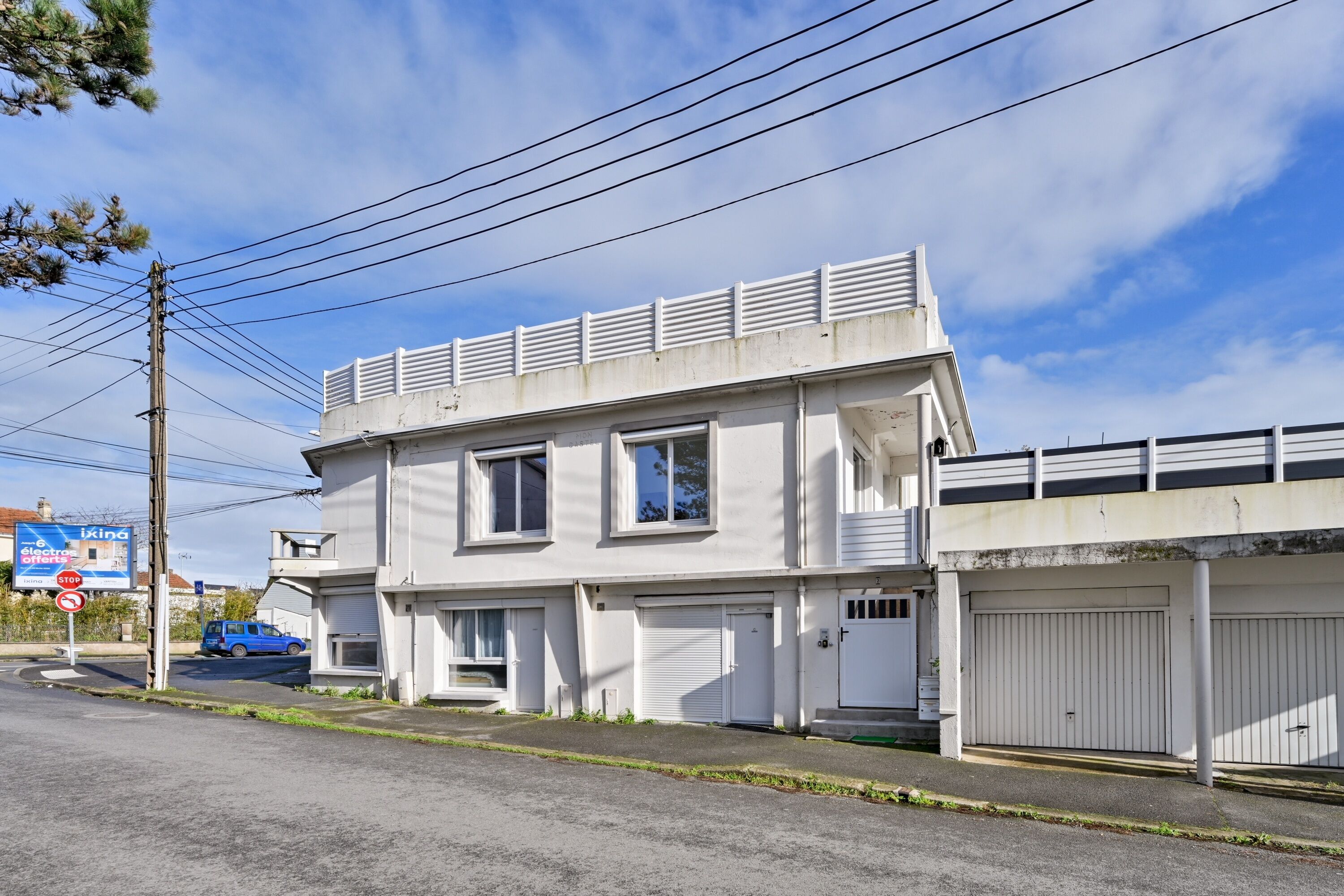 A two-story building with a garage, a stop sign, and a blue car parked in front.