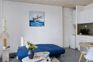 A modern room with a blue bed, a small dining table, a kitchen area, and a painting of a wave on the wall. - Cap Ardoises - Plage à 500m (Saint-Nazaire)