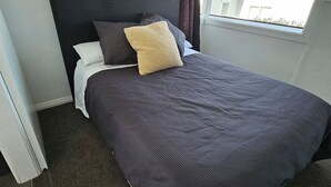 Yhden hengen sänky, jossa on tumma pääty, ikkuna, josta on näkymä rakennukseen, ja verho.