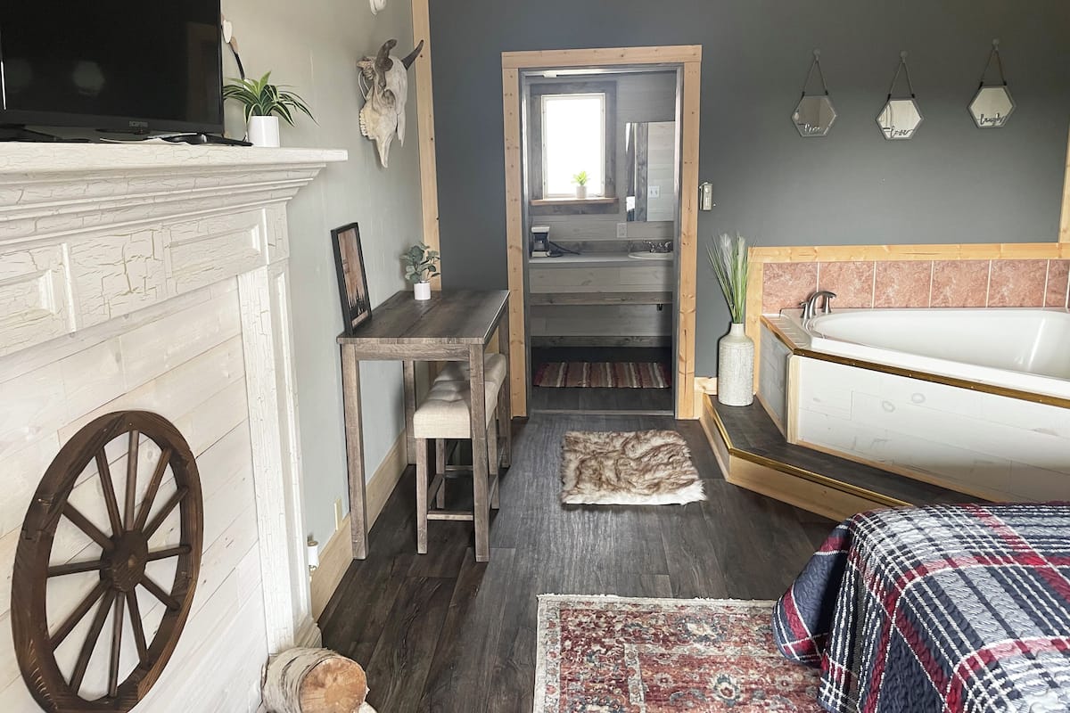 Un dormitorio acogedor con chimenea, una cama grande, un escritorio de madera y un baño visible a través de una puerta abierta.