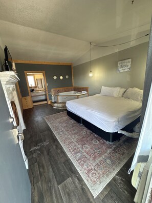 Camera da letto con un ampio letto, una testiera in legno, un bagno piccolo con vasca e un tappeto al pavimento.