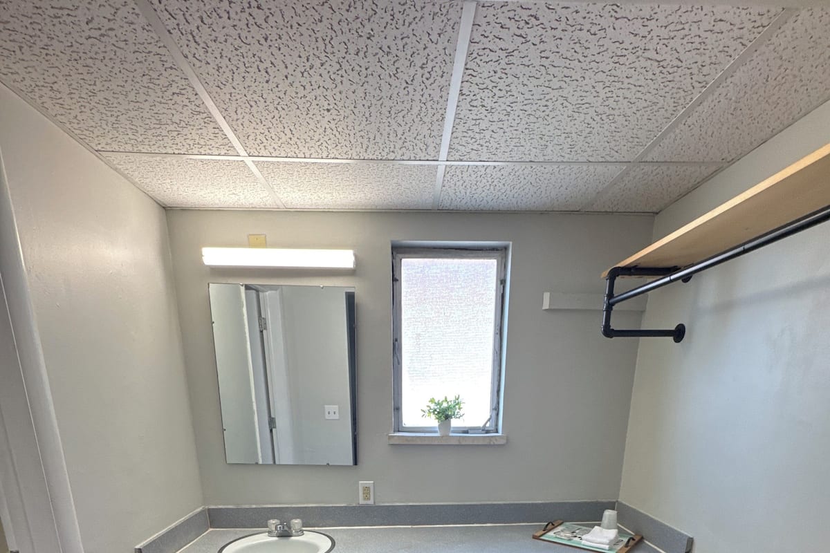 Un baño con un banco de madera, un lavamanos, un espejo y una ventana.