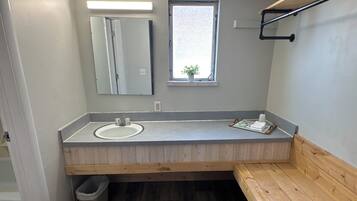 Un baño con un banco de madera, un lavamanos, un espejo y una ventana.