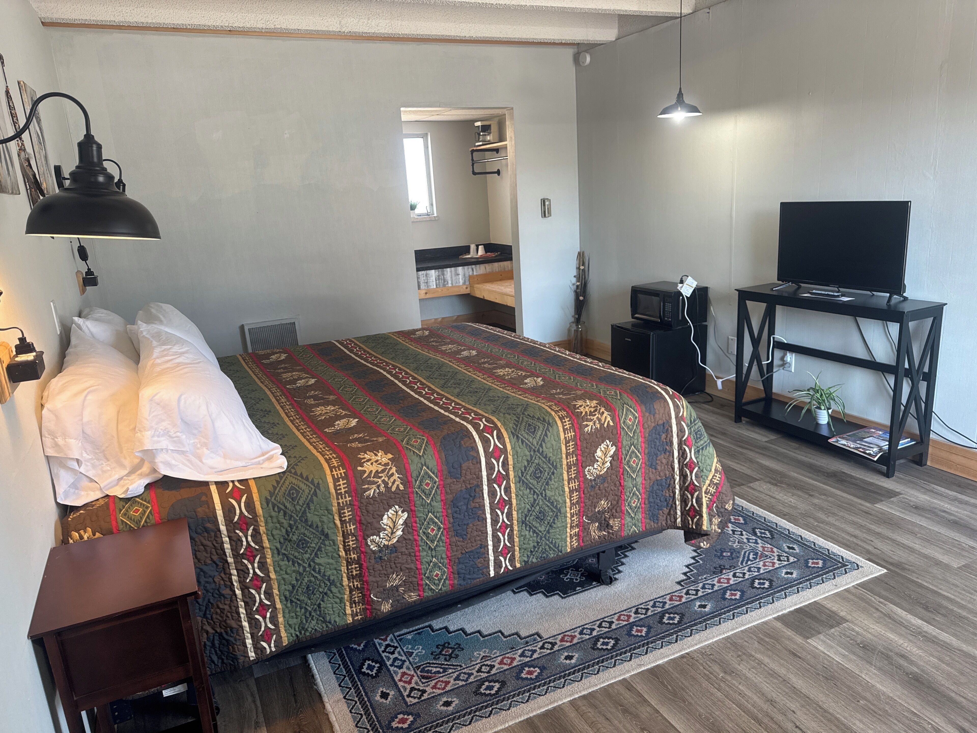 A bedroom with a bed, bedside table, lamp, TV stand, and a small plant.