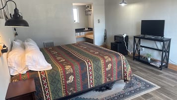 A bedroom with a bed, bedside table, lamp, TV stand, and a small plant.
