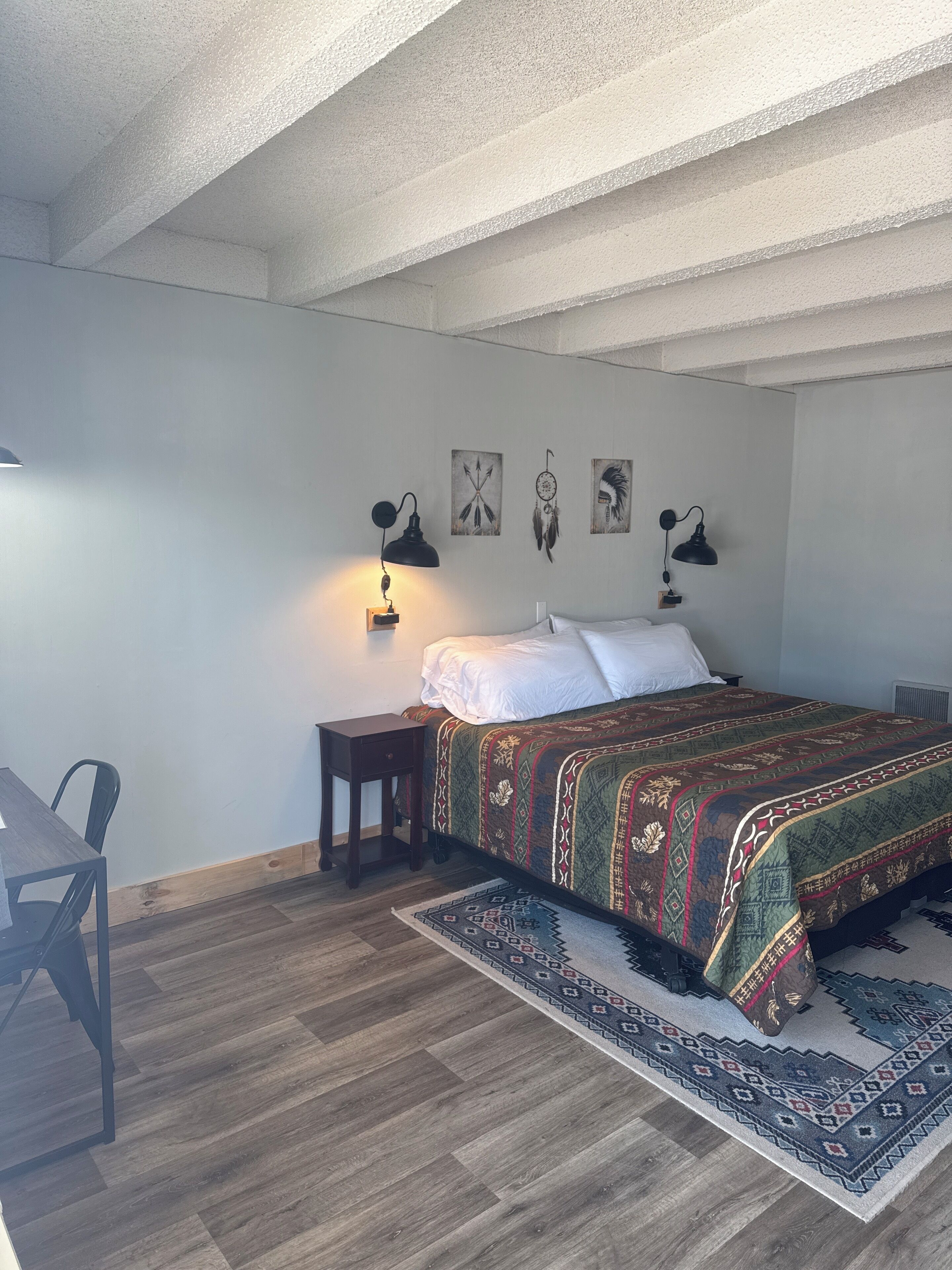 A bedroom with a bed, bedside lamps, a small table, and a chair.