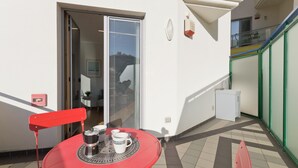 Une table rouge avec une cafetière blanche et des tasses, une chaise rouge et une porte-fenêtre coulissante donnant sur un espace intérieur.