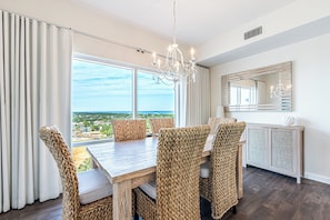 A dining area with wicker chairs, a wooden table, and a chandelier. - Penthouse Unit ~ Gulf View (Miramar Beach)