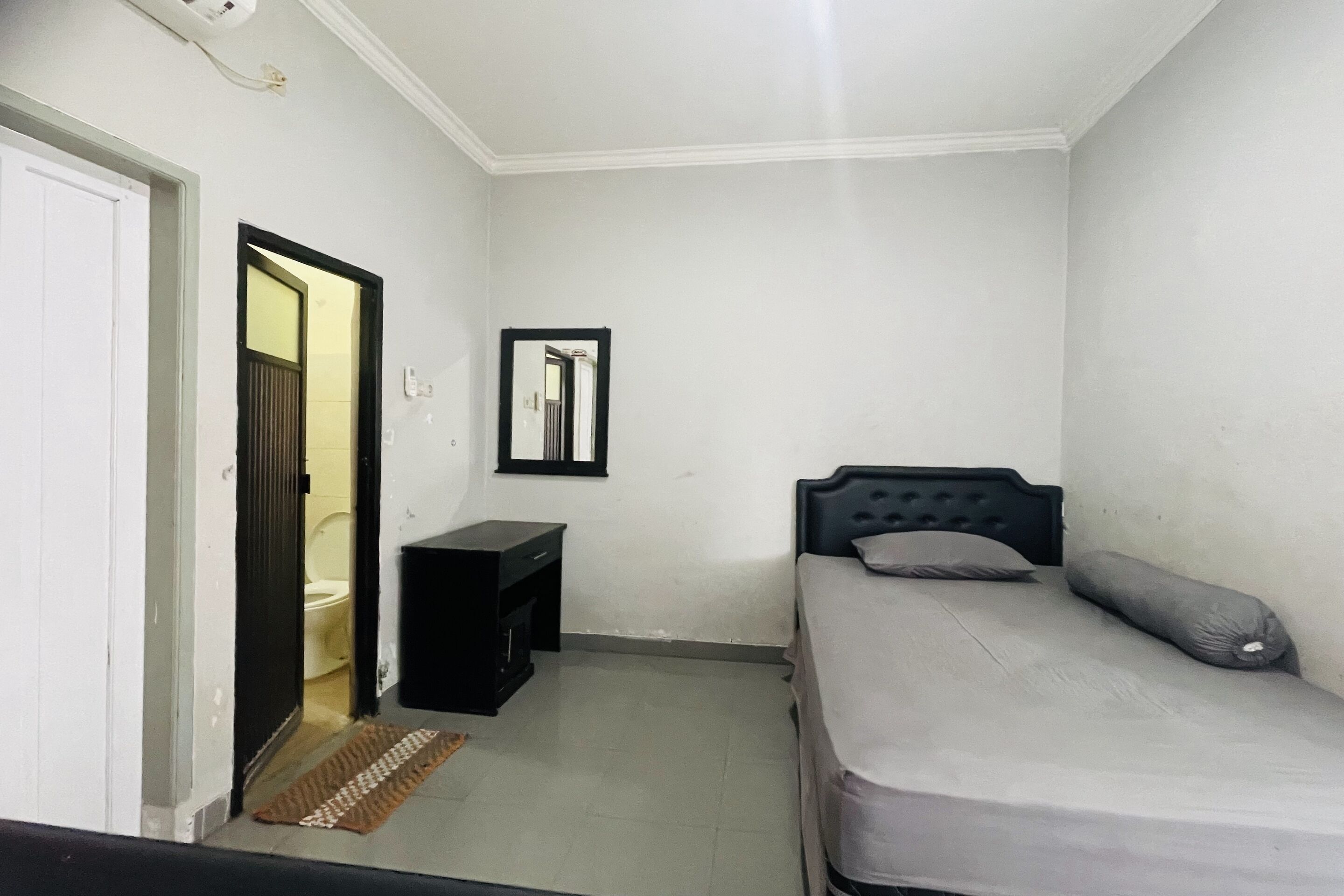 Una habitación pequeña y limpia con cama, mesita de noche y un espejo en la pared.
