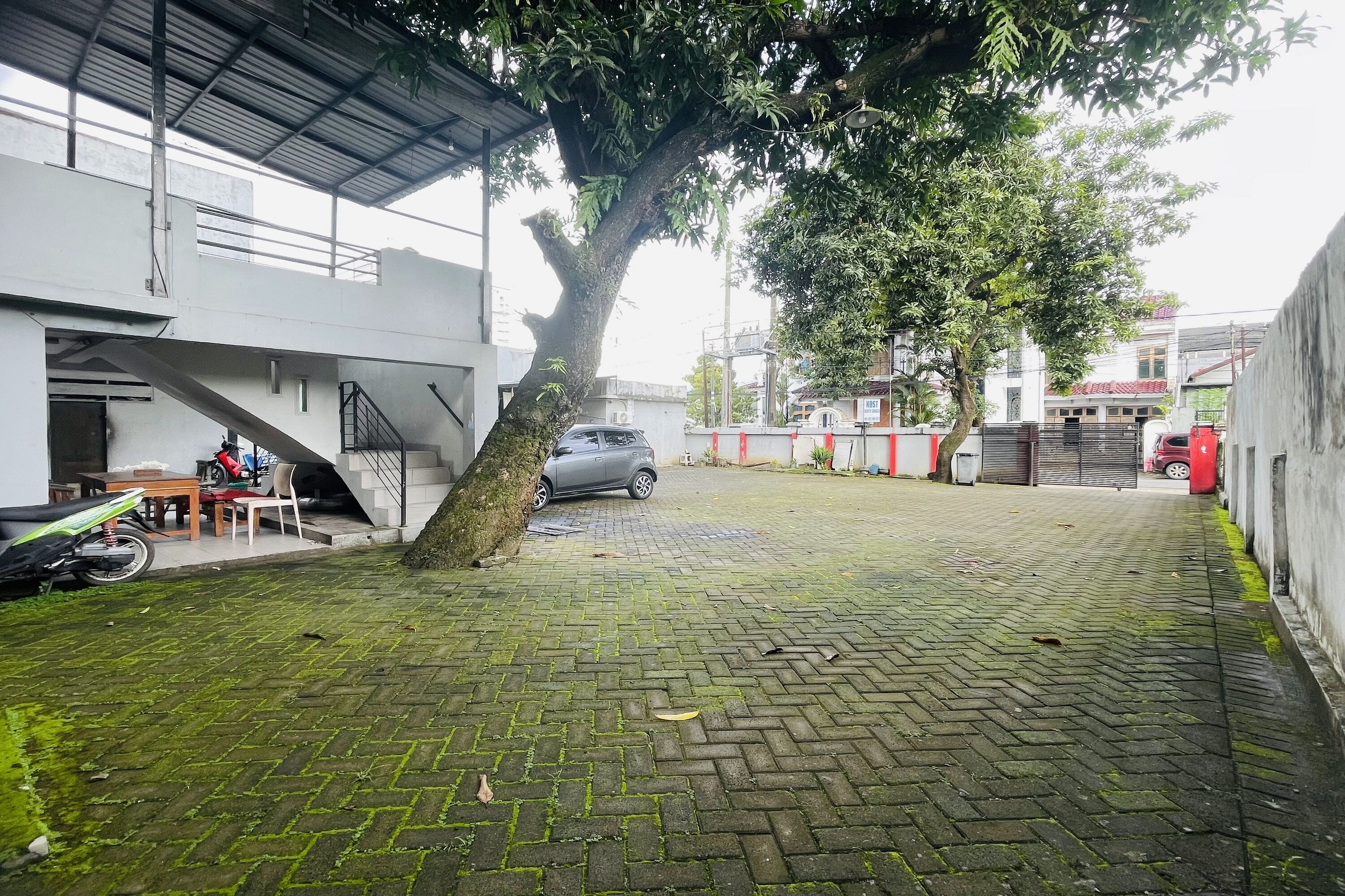 Un patio empedrado con un árbol, una escalera y un coche aparcado.