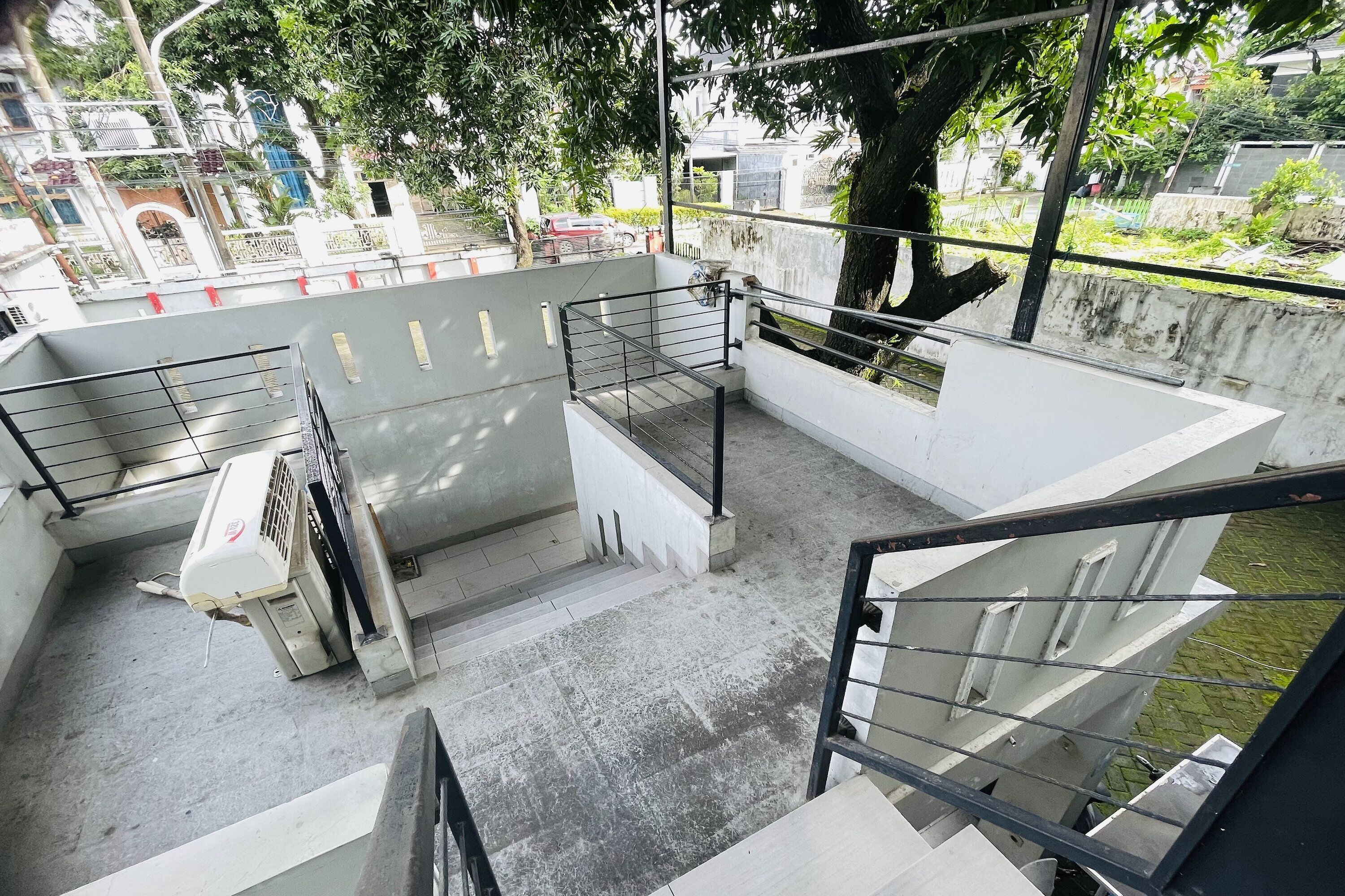 Un espace extérieur à plusieurs niveaux, doté d’escaliers en béton et de rampes en métal, entouré d’arbres et offrant une vue sur un quartier résidentiel.