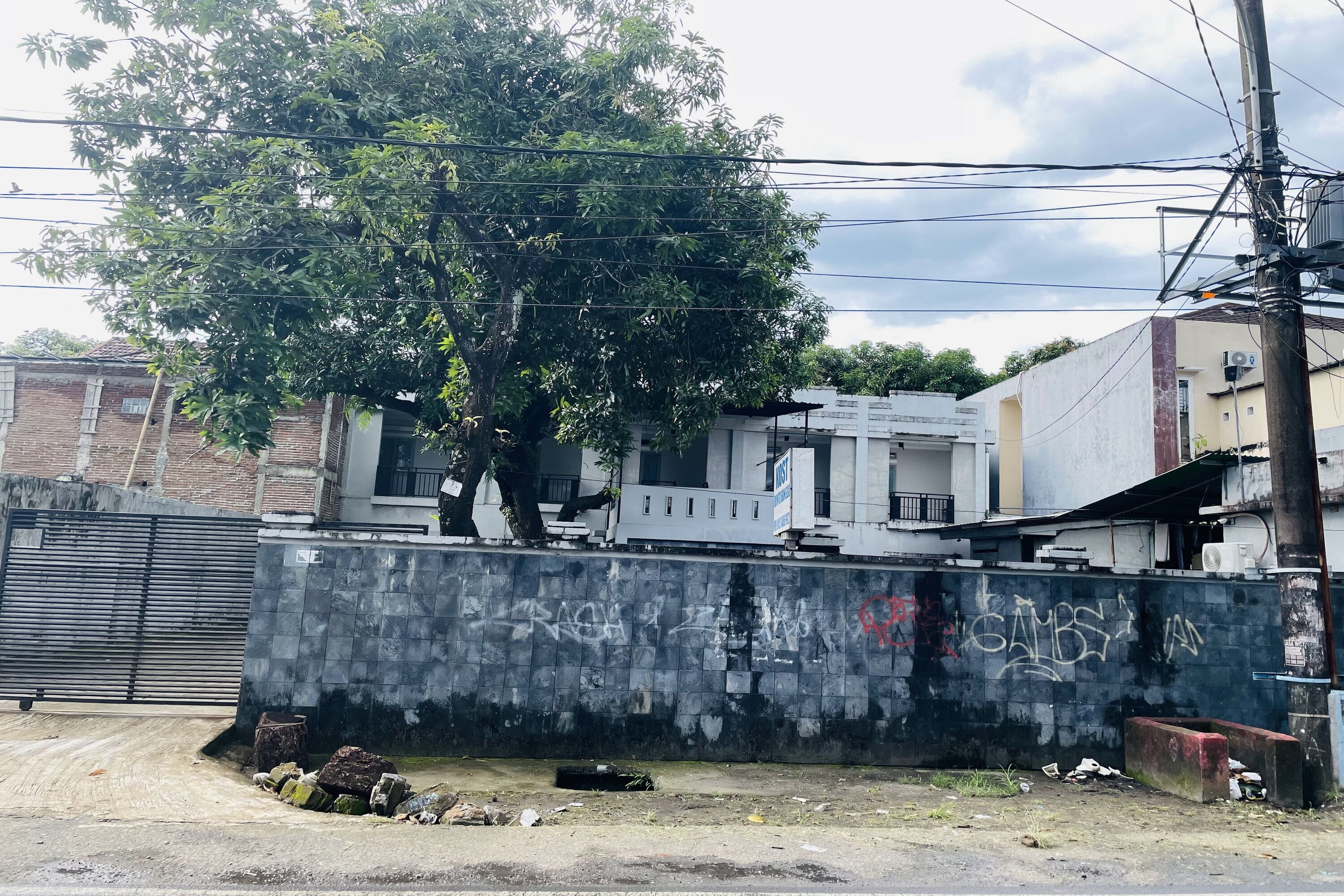 A gated area with graffiti on the wall, a tree, and buildings in the background.