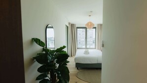 A modern bedroom with a bed, a large mirror, a potted plant, and a view of buildings through the window. - Large apartment with balcony, 3 BR and 2 Bathrooms (Antwerpen)