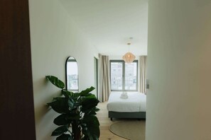 A modern bedroom with a bed, a large mirror, a potted plant, and a view of buildings through the window. - Large apartment with balcony, 3 BR and 2 Bathrooms (Antwerpen)
