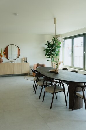 A modern dining area with a long table, chairs, a round mirror, a potted plant, and a hanging light fixture. - Large apartment with balcony, 3 BR and 2 Bathrooms (Antwerpen)