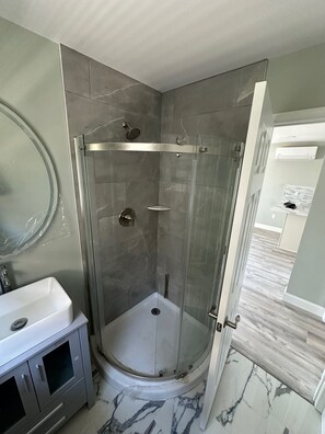 Un baño moderno con ducha envuelta en vidrio, un lavabo blanco y suelo de mármol.