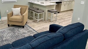 Een moderne keuken met witte kasten, een centraal eiland en een ingebouwde vaatwasser. In de woonruimte staat een beige fauteuil en een blauwe bank.